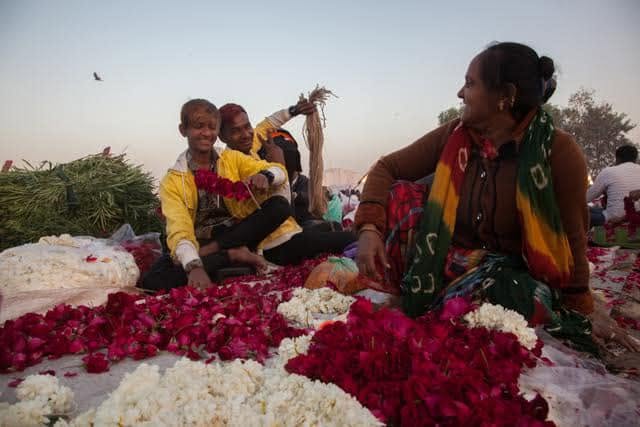 Flower sellers sitting among piles of roses and jasmine before sunrise at Ahmedabad flower market.