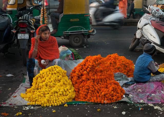 A woman selling marigold flowers beside a busy street in Ahmedabad.