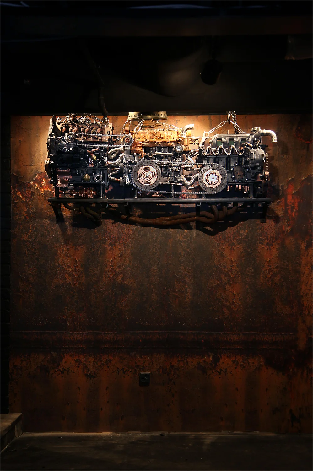 Machines from Hell by Magi Viljanen, a large assemblage of engines, gears and pipes mounted against a rust-coloured wall.